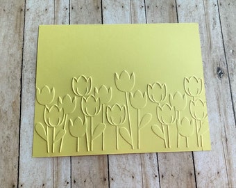 May include: A yellow card with a row of embossed tulips along the bottom edge.