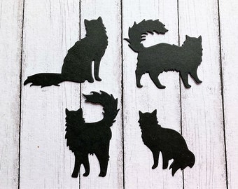 May include: Four black paper cat silhouettes on a white wood background. The cats are in various poses, including sitting, standing, and lying down.