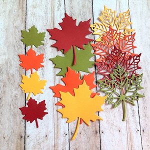 May include: Assortment of fall-themed paper leaves in various colors, including red, orange, yellow, and green. The leaves are cut in a variety of shapes and sizes, and some have a delicate, lacy design.