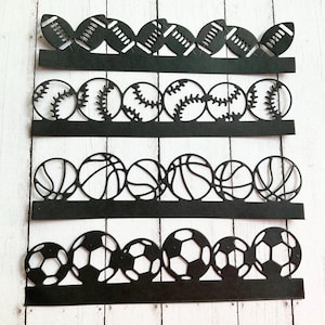 May include: Black paper cutouts of various sports balls, including footballs, baseballs, basketballs, and soccer balls. The cutouts are arranged in rows, with each row featuring a different type of ball. The design is simple and graphic.