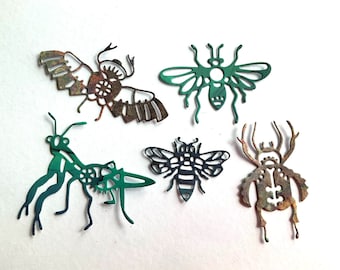 May include: Five metal insect cutouts with intricate details. The insects are a dragonfly, a bee, a beetle, a mantis, and a moth. The cutouts are painted in shades of green and brown.