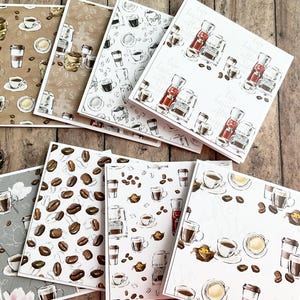 Könnte beinhalten: Eine Sammlung quadratischer Karten mit Kaffeemotiven. Die Karten zeigen Illustrationen von Kaffeetassen, Bohnen und Kaffeemaschinen in verschiedenen Stilen und Farben, darunter Braun, Weiß und Rot. Die Karten sind auf einer Holzoberfläche angeordnet.
