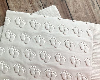 May include: White paper napkins with an embossed pattern of tiny footprints. The napkins are folded and stacked.