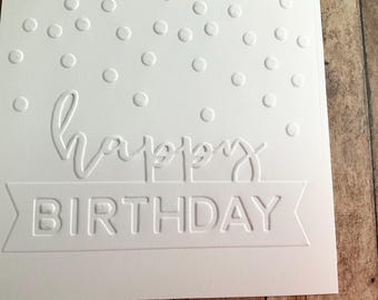 May include: White birthday card with embossed text and polka dots. The words "happy" and "birthday" are prominently displayed. The card has a simple, elegant design, perfect for celebrating a special day.