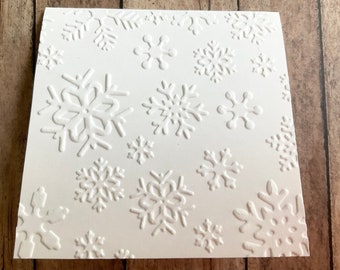 May include: White cardstock with a raised embossed pattern of snowflakes. The snowflakes are of various sizes and shapes.