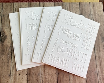 May include: Four white embossed cards with different thank you messages. The cards have a raised, textured design and include phrases like "Thanks so much", "A big thank you", and "You're the best!"