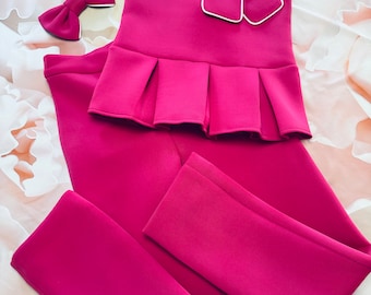 May include: A pink sleeveless top with a white trim and a large pink bow. The top is paired with matching pink pants.