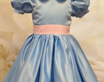 May include: A light blue dress with a pink bow and a pink sash. The dress has a peter pan collar and puffed sleeves.
