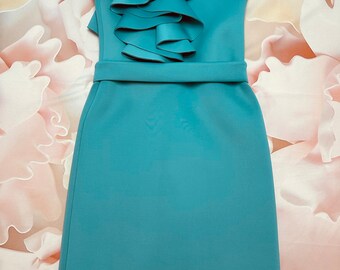 May include: A teal blue sleeveless dress with a large ruffle detail on the left shoulder. The dress has a fitted bodice and a straight skirt.