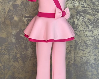 May include: A pink and hot pink two-piece outfit for a girl. The top has a puffed sleeve, a bow, and a skirt. The pants are long and flared.