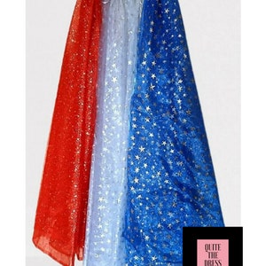 May include: A red, white, and blue cape with gold stars. The cape is made of sheer fabric and has a white satin lining. The cape is trimmed with a red, white, and blue ribbon.