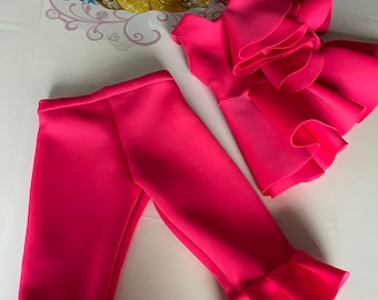 May include: A pink two-piece outfit for a child, featuring a ruffled top and pants with ruffled hems.