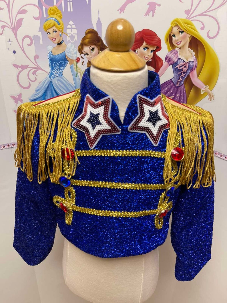 May include: A blue glittery jacket with gold trim and red, white and blue star embellishments. The jacket has long sleeves and a cropped length.
