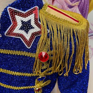 May include: A blue sequined jacket with gold trim and a red star on the front. The jacket has a gold fringe on the shoulder and red and blue jewels.