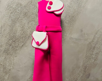 May include: A pink jumpsuit with a white collar and a white purse with a pink button. The jumpsuit has a wide leg and a belt.