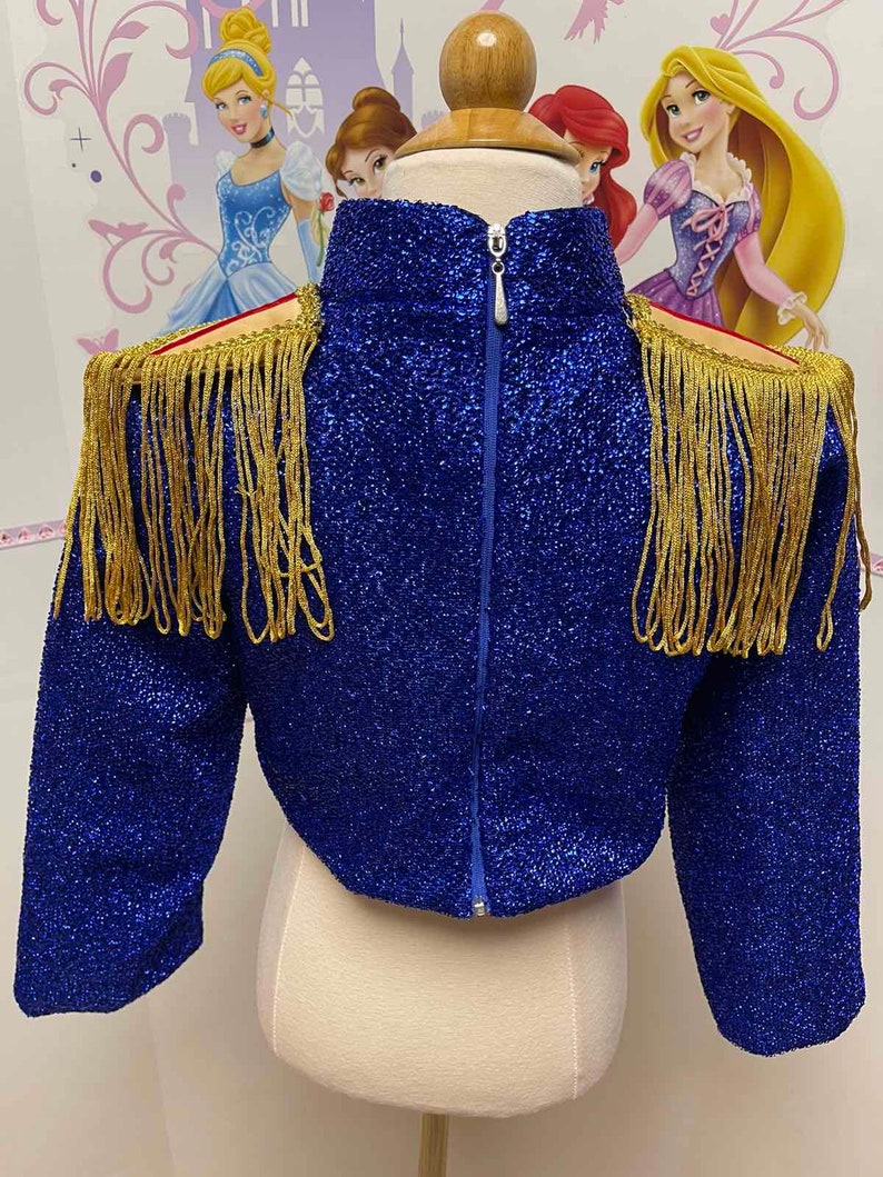 May include: A blue sparkly jacket with gold fringe trim on the shoulders and sleeves. The jacket has a zipper closure at the back.