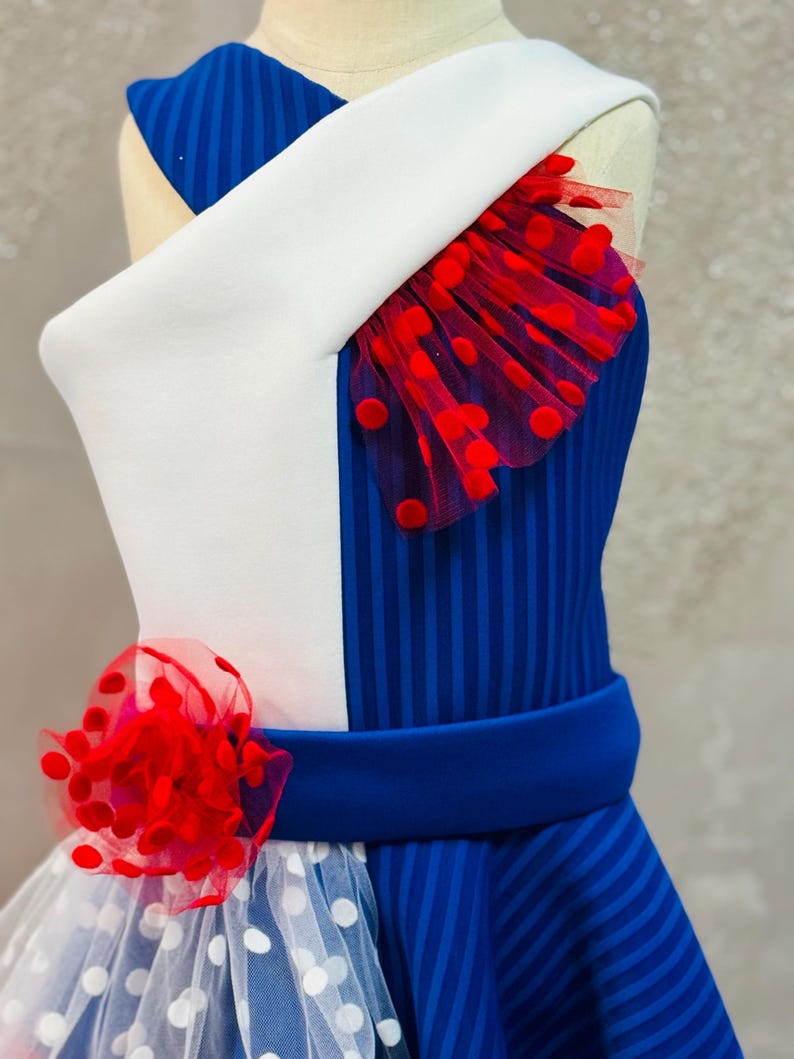 May include: A blue and white dress with red polka dots. The dress has a white bodice with a blue and white striped skirt. The dress has a red bow on the front.