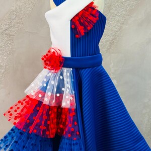May include: A blue and white dress with red polka dot tulle accents. The dress has a white bodice with a blue and white striped panel and a blue skirt with a layered tulle skirt.