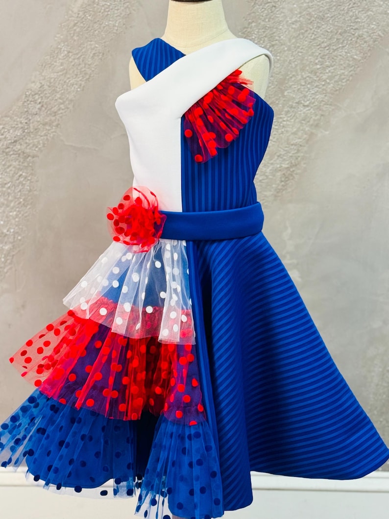 May include: A blue and white dress with red polka dot tulle accents. The dress has a white bodice with a blue and white striped panel and a blue skirt with a layered tulle skirt.