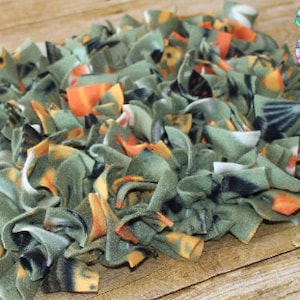 May include: A green, orange, and white fleece dog enrichment mat. The mat is made of strips of fleece fabric that are knotted together. This mat is designed to provide dogs with a stimulating and engaging activity.