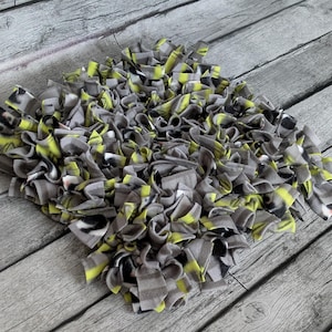 May include: A handmade, square-shaped pet bed made of gray, black, and yellow fleece strips. The fleece strips are knotted together to create a textured, shaggy appearance. The bed is designed for small pets.