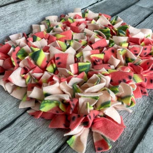 May include: A pink and green watermelon-patterned dog bed with a variety of fabric strips for dogs to play with.