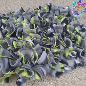 May include: A handmade pet bed made of gray, black, and lime green fleece strips. The strips are knotted together to create a soft, textured surface. The pet bed is designed to provide comfort and warmth for small animals.