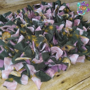 May include: A handmade, round rug composed of layered fabric strips in shades of green, pink, and yellow. The rug has a shaggy texture and is placed on a wooden surface. This item is suitable for home decor.