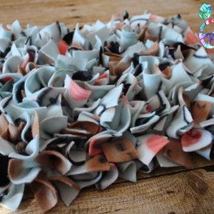 May include: A handmade pet snuffle mat in a rectangular shape. The mat is made of soft fleece strips in light blue, brown, black, and pink. The mat is designed to stimulate a pet's sense of smell.