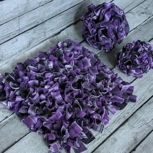 May include: A set of three handmade items: a square rug and two round decorative pieces. The items are made of a soft, textured fabric in shades of purple, black, and white. The rug is approximately 18 inches square.