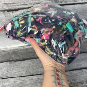 May include: A clear plastic bag filled with colorful fabric scraps. The fabric is a mix of blue, pink, green, and yellow.