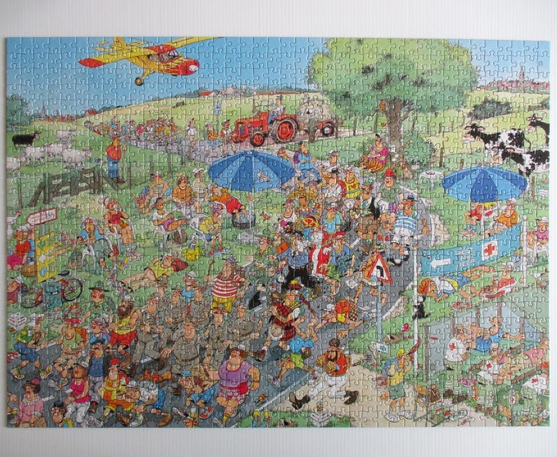 May include: A colorful jigsaw puzzle depicting a busy outdoor marathon scene with numerous runners, spectators, a red tractor, a yellow airplane in the sky, blue umbrellas, and a medical tent with a red cross sign on a green grassy landscape.