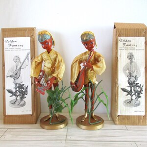May include: Two vintage Golden Fantasy hand painted figurines of elves playing musical instruments. The elves are dressed in gold and have red faces. They are standing on a green base with leaves. The boxes are brown with gold lettering and show the elves playing different instruments.