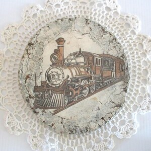 May include: A vintage ceramic plate with a distressed white glaze features a hand-painted image of a brown and black steam locomotive train. The train is on a track with a white background.