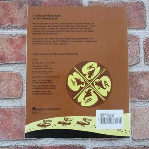 May include: The back cover of a paperback book with a brown background and a yellow design of four stylized birds. The book title is "The Desert is Theirs" and the author is Byrd Baylor. The book is a Caldecott Honor Book and an ALA Notable Book. Other books by the same author are listed on the back cover.