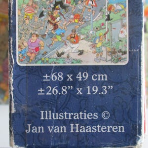 May include: A rectangular puzzle box featuring a colorful cartoon illustration by Jan van Haasteren. The box displays dimensions of approximately 26.8 inches by 19.3 inches. The dark blue packaging includes the text Illustraties Jan van Haasteren.