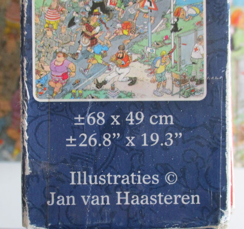 May include: A rectangular puzzle box featuring a colorful cartoon illustration by Jan van Haasteren. The box displays dimensions of approximately 26.8 inches by 19.3 inches. The dark blue packaging includes the text Illustraties Jan van Haasteren.