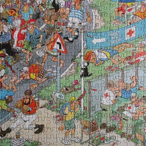 May include: A colorful jigsaw puzzle featuring a busy cartoon scene of hikers and runners on a road. A blue banner with a red cross and the text REST AND HELP hangs above a medical station where figures in white uniforms assist others.