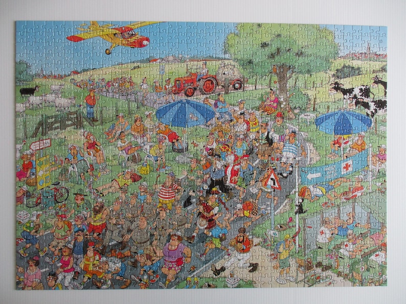 May include: A jigsaw puzzle featuring a colorful, busy cartoon illustration of a crowded outdoor event. The scene includes a yellow airplane flying overhead, a red tractor, blue umbrellas, and numerous people walking along a road.