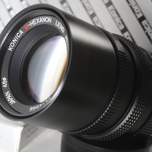 May include: A black Konica M-Hexanon lens with the text "JAPAN 466" and "KONICA M-HEXANON LENS" printed on the side.