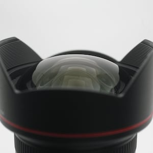 May include: A black camera lens with a red ring around the edge. The lens is pointed upwards and the front element is visible.