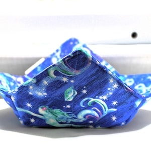 May include: A blue fabric bowl with a mermaid and star pattern. The bowl is folded into a triangular shape.
