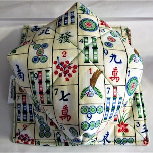 May include: A white fabric square with a pattern of mahjong tiles, numbers, and Chinese characters. The fabric is quilted and has a 3D effect. The fabric is folded into a cube shape.