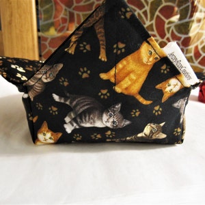 May include: Black fabric bowl with a cat paw print pattern and a variety of cats printed on it. The bowl is folded and has a white tag that says "Jersey Rose Creations".
