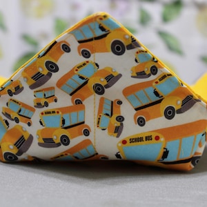 Peut inclure: Un bol en tissu jaune avec un motif de bus scolaire. Le bol est plié et a une doublure jaune.