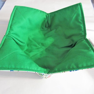 May include: A green quilted bowl liner with a white and blue patterned fabric lining. The liner is folded and ready to be used.