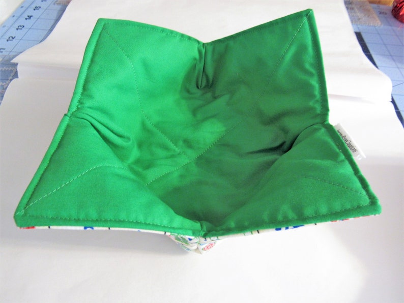 May include: A green quilted bowl liner with a white and blue patterned fabric lining. The liner is folded and ready to be used.