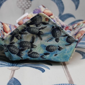 May include: A fabric bowl with a sea turtle design. The bowl is blue and white with a pattern of sea turtles swimming in the ocean. The interior of the bowl has a seashell pattern.