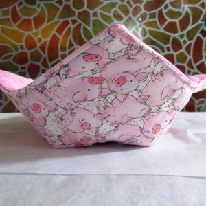 May include: A pink fabric bowl with a pattern of pink pigs on a white background. The bowl is folded and has a square shape.
