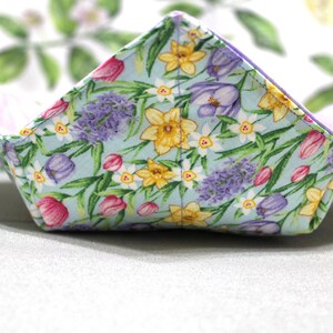 May include: A light blue fabric bowl with a floral pattern featuring tulips, daffodils, and purple flowers. The bowl is folded and has a white background.